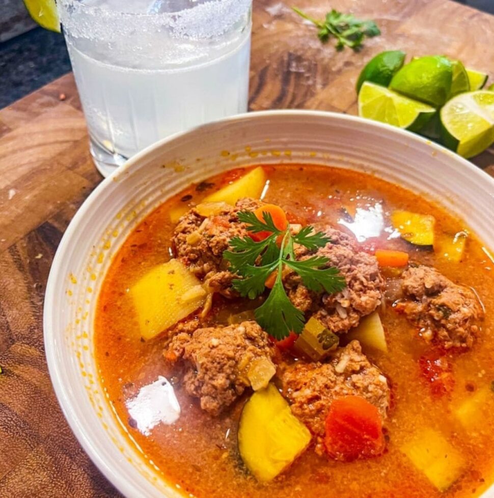 picture of albondigas meatball soup with margarita and lime slices in the background