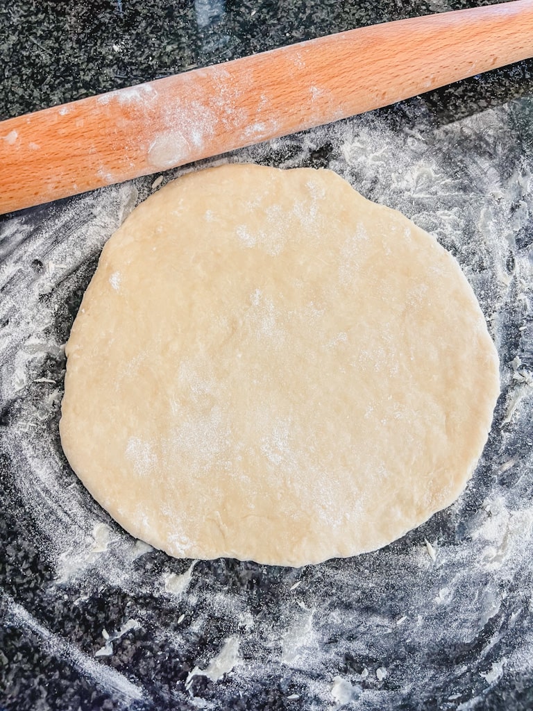 picture of slightly rolled out simple butter pie crust with flour and rolling pin