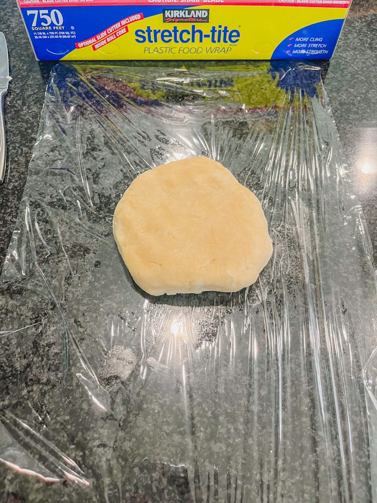 dough in a flat disc shape on saran wrap 
