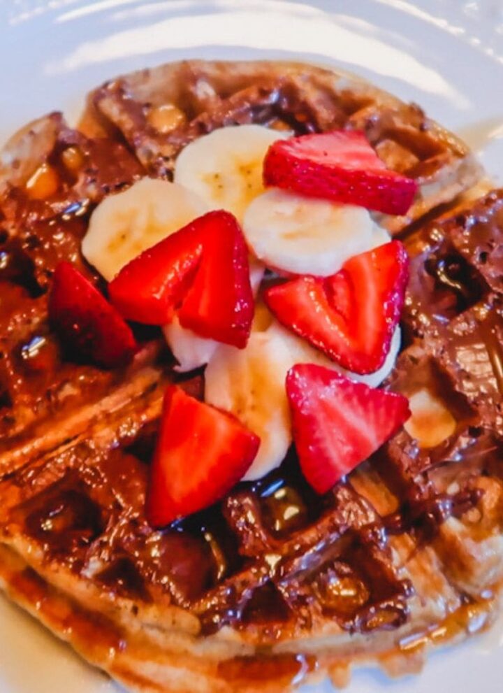 close up of homemade belgian waffle with nutella, bananas, strawberries, and maple syrup