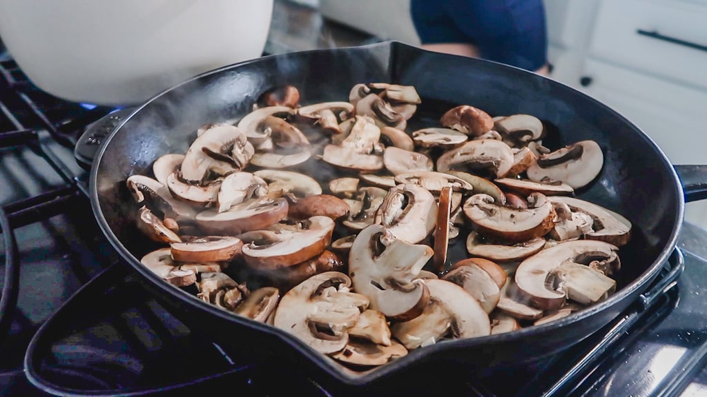 close up of cut mushrooms sauteeing in pan on stove