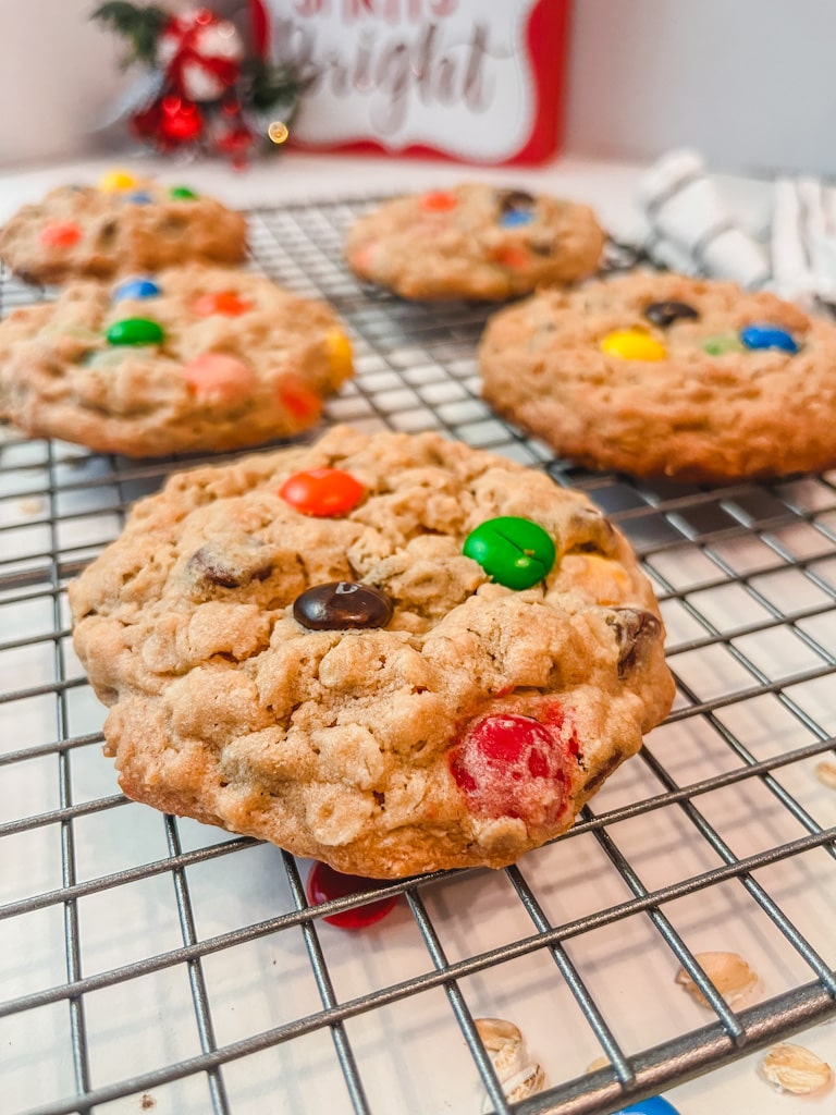 close up picture of the best m&m monster cookies on a cooling rack with Christmas decorations blurred out in the background