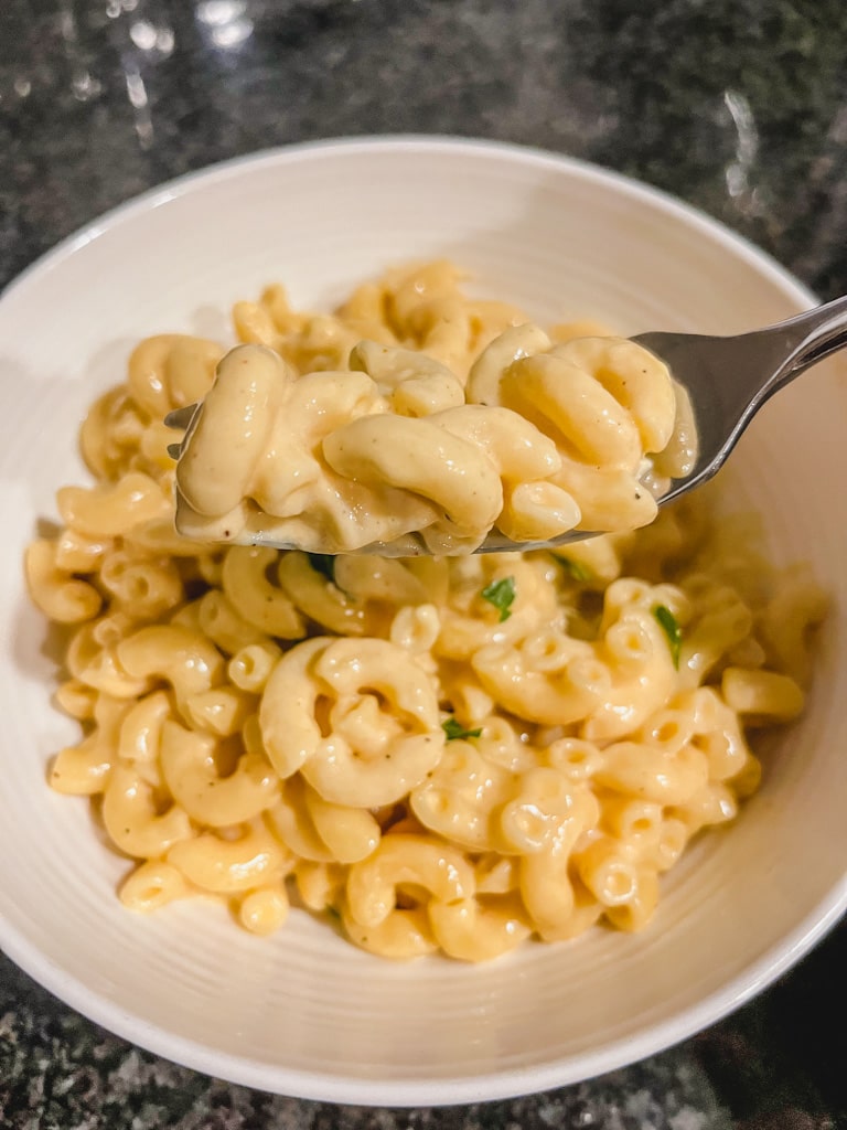 close up of creamy mac and cheese on a fork over bowl of macaroni