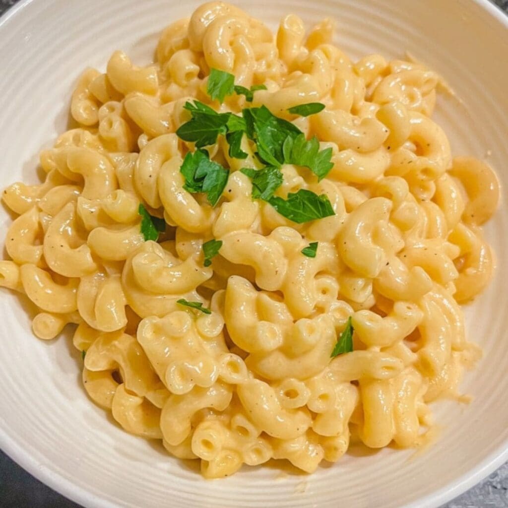 close up picture of creamy stove top macaroni and cheese in white bowl with chopped parsley on top