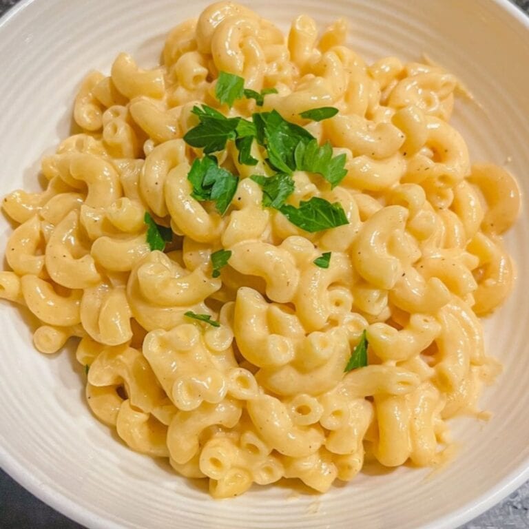 close up picture of creamy stove top macaroni and cheese in white bowl with chopped parsley on top