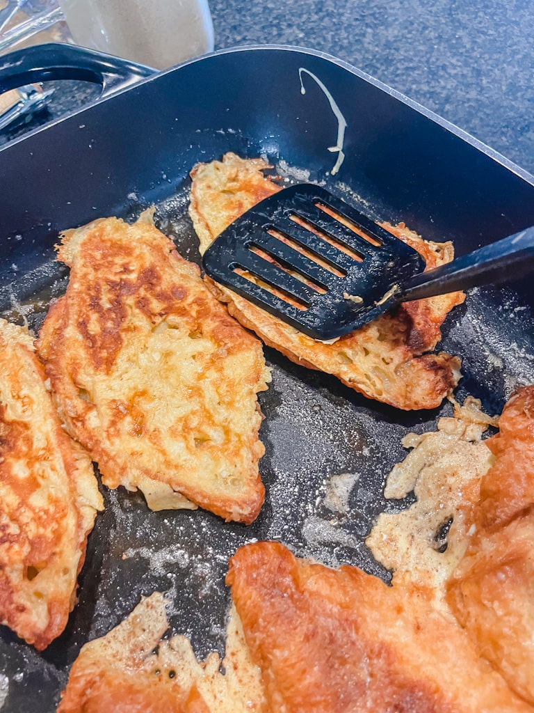 black spatula pressing down on croissant french toast to flatten to help caramelize
