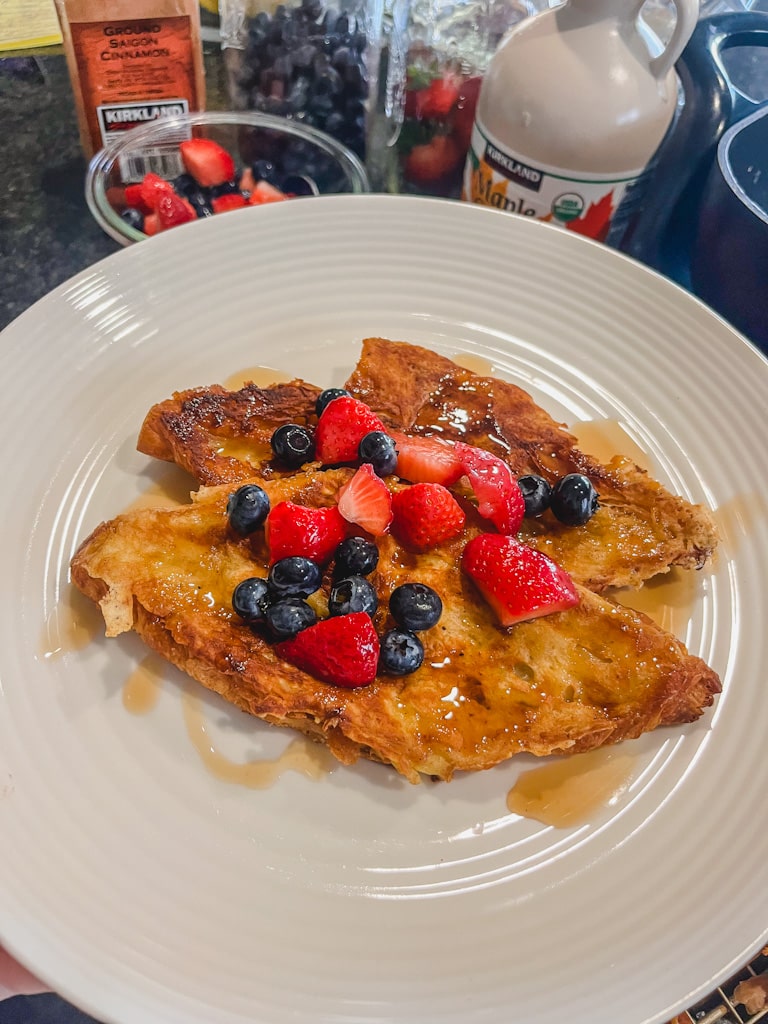 butter croissant french toast with fresh berries on top and drizzle of maple syrup