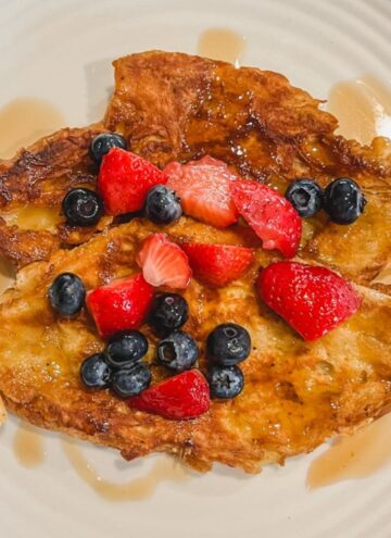 croissant french toast on a white plate with strawberries, blueberries and maple syrup on top
