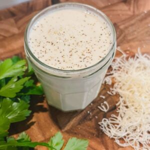 quick Alfredo sauce in jar on cutting board with fresh parsley and grated Parmesan cheese