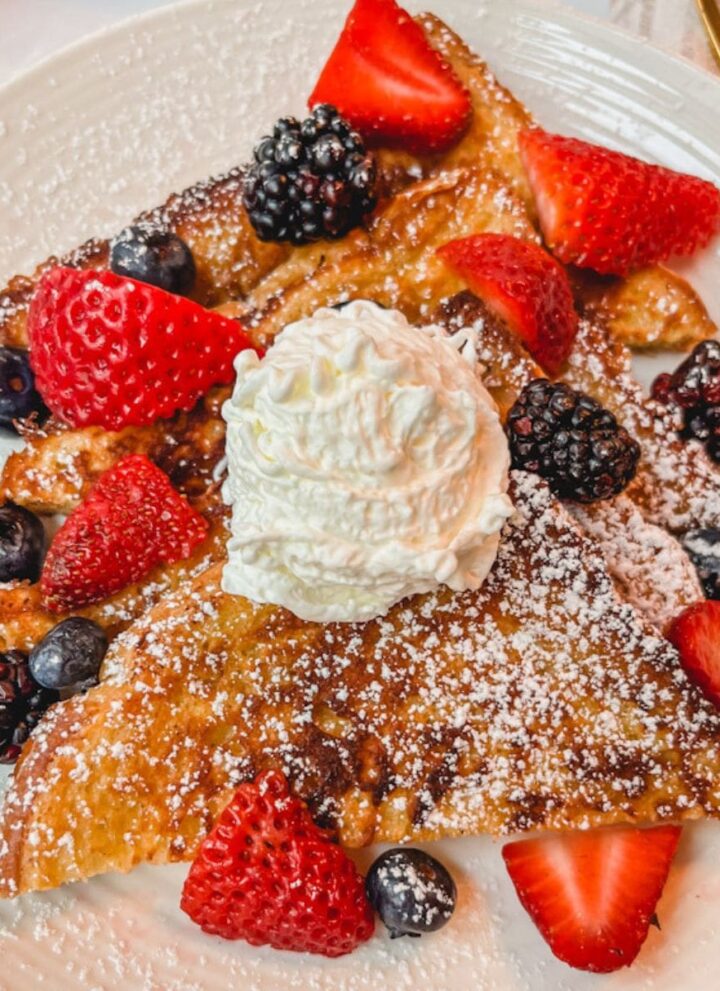 the best brioche cinnamon french toast sliced on a plate served with fresh berries and a dollop of whipped cream on top.