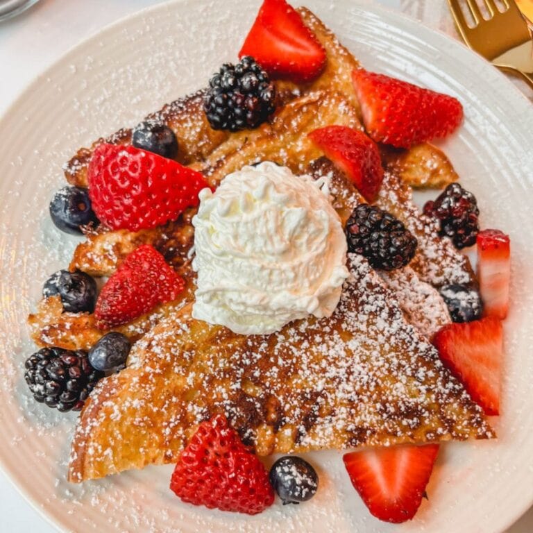 the best brioche cinnamon french toast sliced on a plate served with fresh berries and a dollop of whipped cream on top.