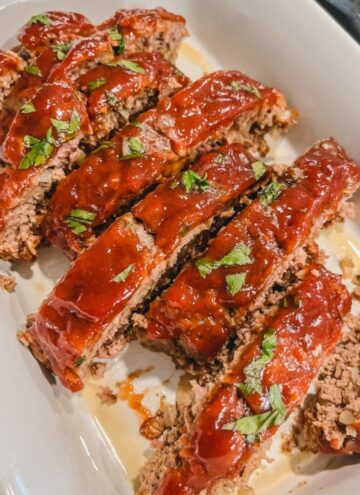 classic ground beef meatloaf cut into 8 slices in a white casserole baking dish ready to serve and eat.