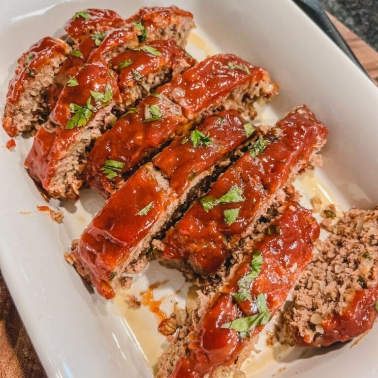 classic ground beef meatloaf cut into 8 slices in a white casserole baking dish ready to serve and eat.