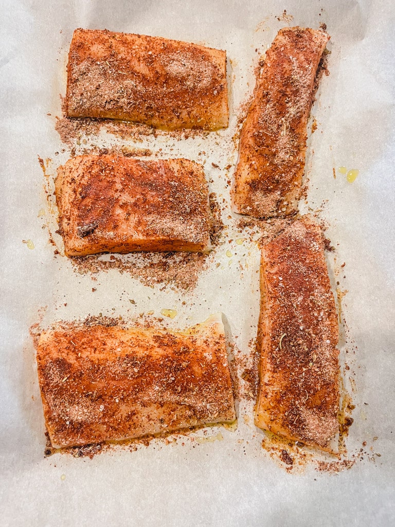 seasoning rub has been rubbed into the 5 fillets of cod on prepared baking sheet ready to be baked in the oven.