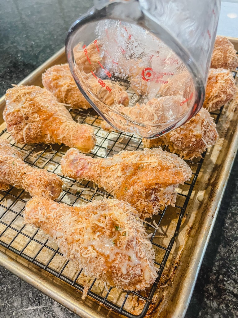 pouring melted butter over breaded chicken drumsticks