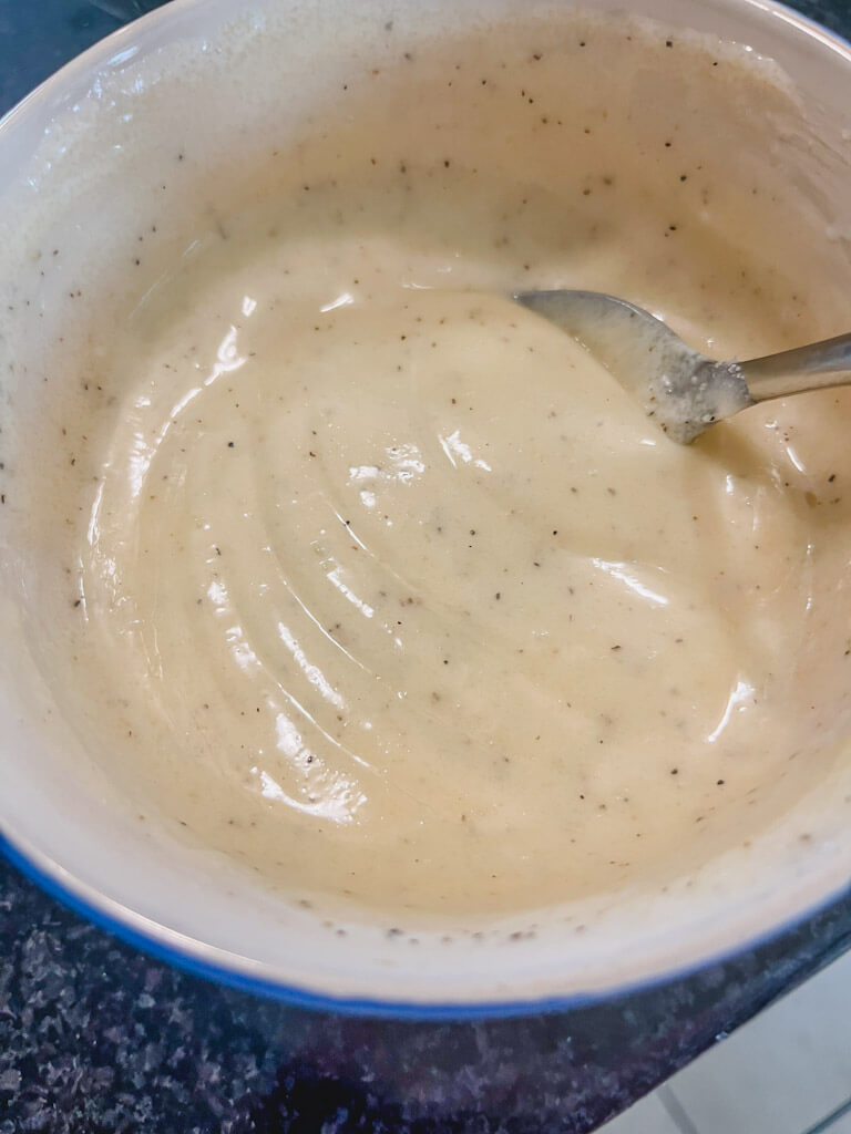 tangy creamy dressing in a blue bowl ready to be poured over broccoli apple salad.