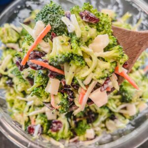 close up of broccoli apple salad with cranberries on a wooden spoon ready to serve.