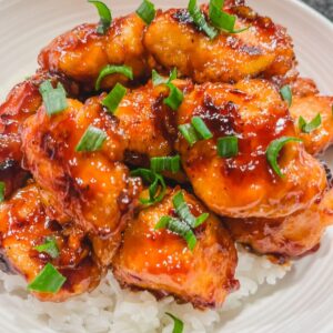 sticky honey chicken garnished with green onions on steamed white rice.