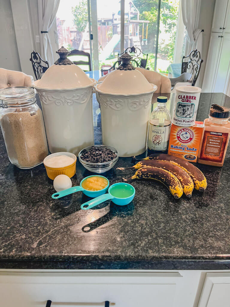 ingredients for dark chocolate chip banana muffins laid out on a black countertop.