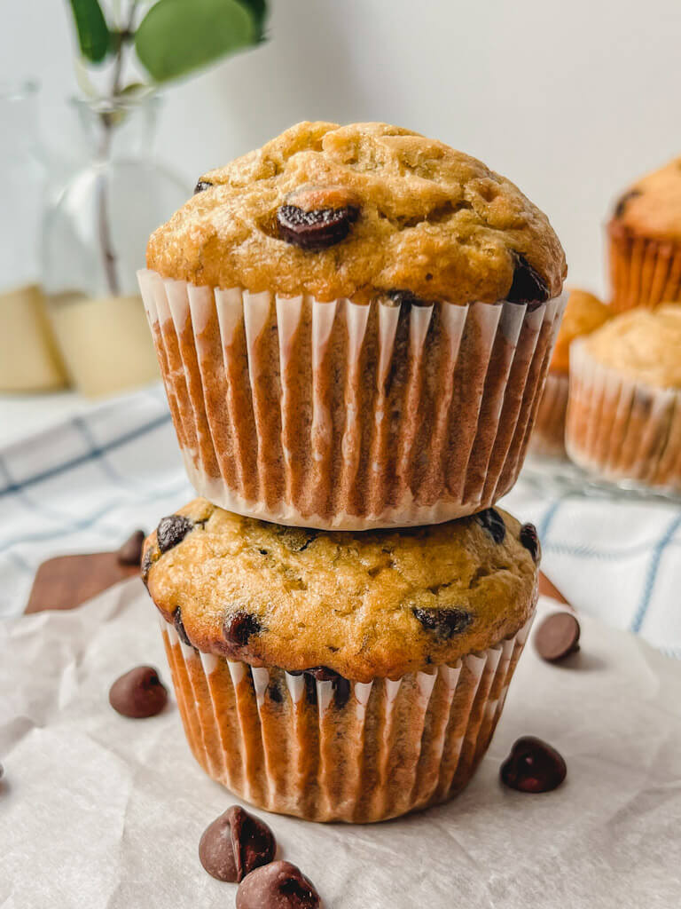 two banana muffins stacked on top of each other with loose chocolate chips surrounding muffins. 