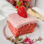 close up of fresh strawberry cake on a rose plate with strawberries in the background.