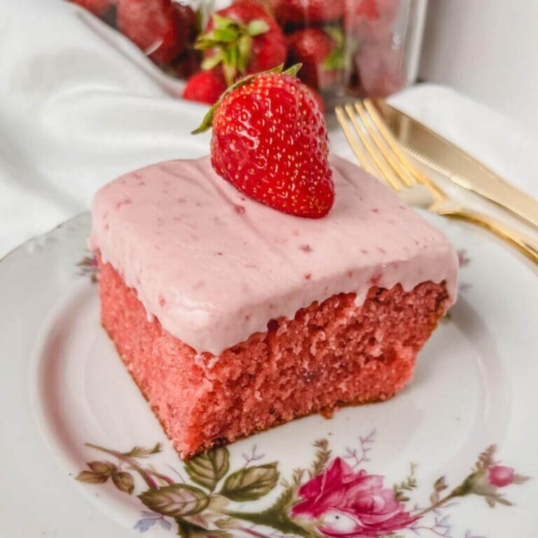 close up of fresh strawberry cake on a rose plate with strawberries in the background.