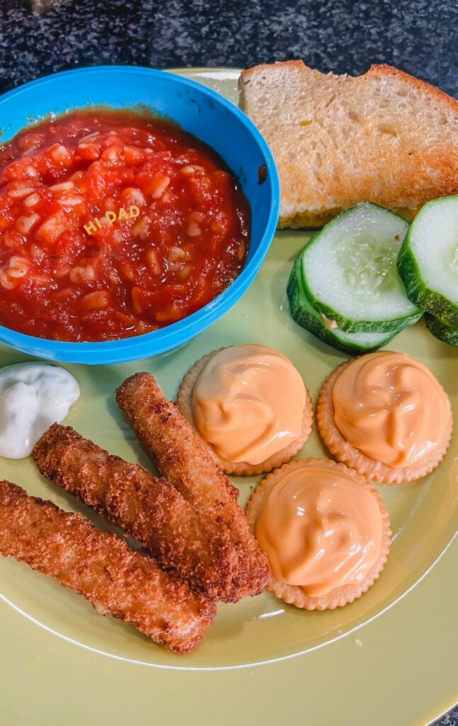 hi dad tomato soup, cucumber slices, grilled cheese, fish sticks, and cheese crackers on a yellow plate for a goofy movie dinner night.