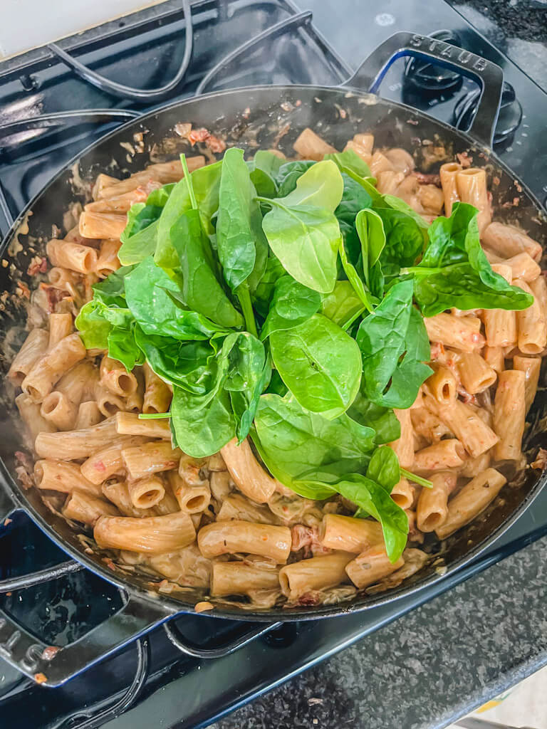 fresh spinach going into a one-pot sun-dried tomato and chicken pasta dinner.