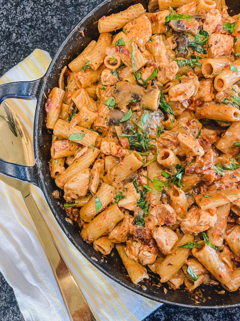 one pot sun-dried tomato and chicken pasta in a large blue skillet next to a gold serving spoon.