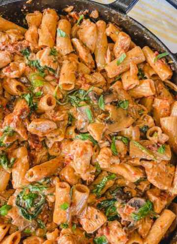 one pot sun-dried tomato and chicken pasta dinner in a large skillet next to a white and yellow kitchen towel.