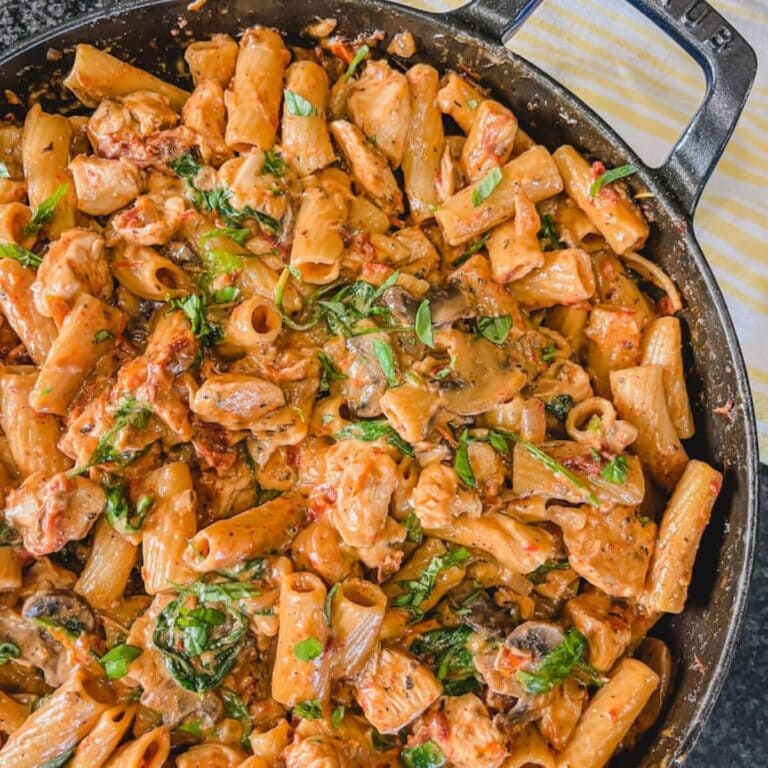 one pot sun-dried tomato and chicken pasta dinner in a large skillet next to a white and yellow kitchen towel.