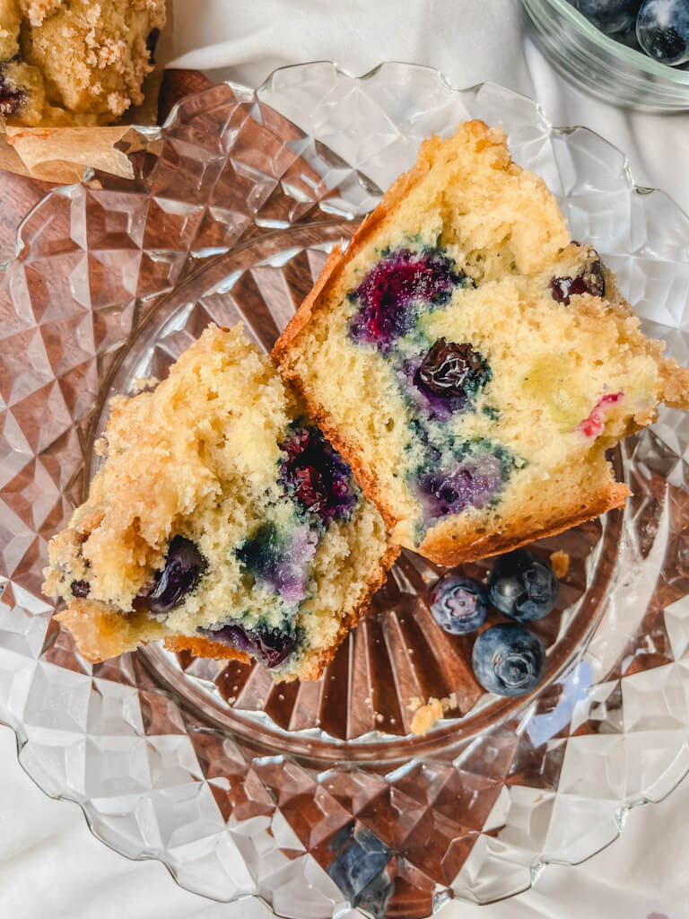 a blueberry muffin cut in half on a glass plate.