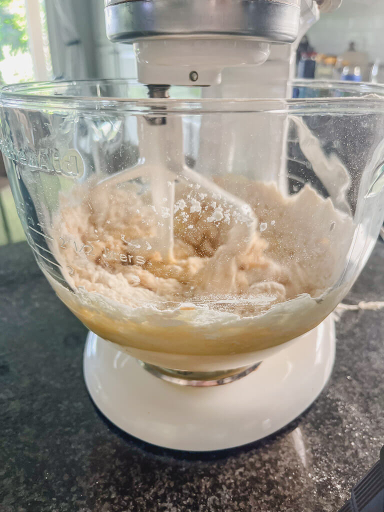 dry ingredients being added to a clear glass mixing bowl in a stand mixer.