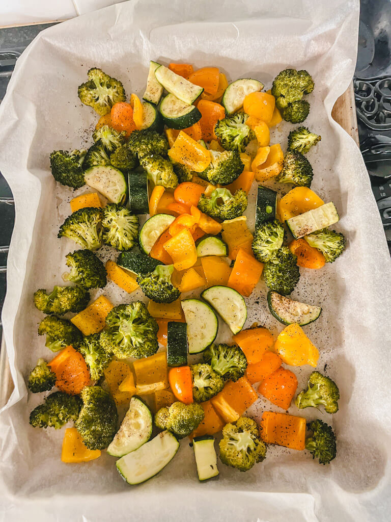 broccoli, zucchini and bell peppers on a baking sheet after being roasted in the oven.