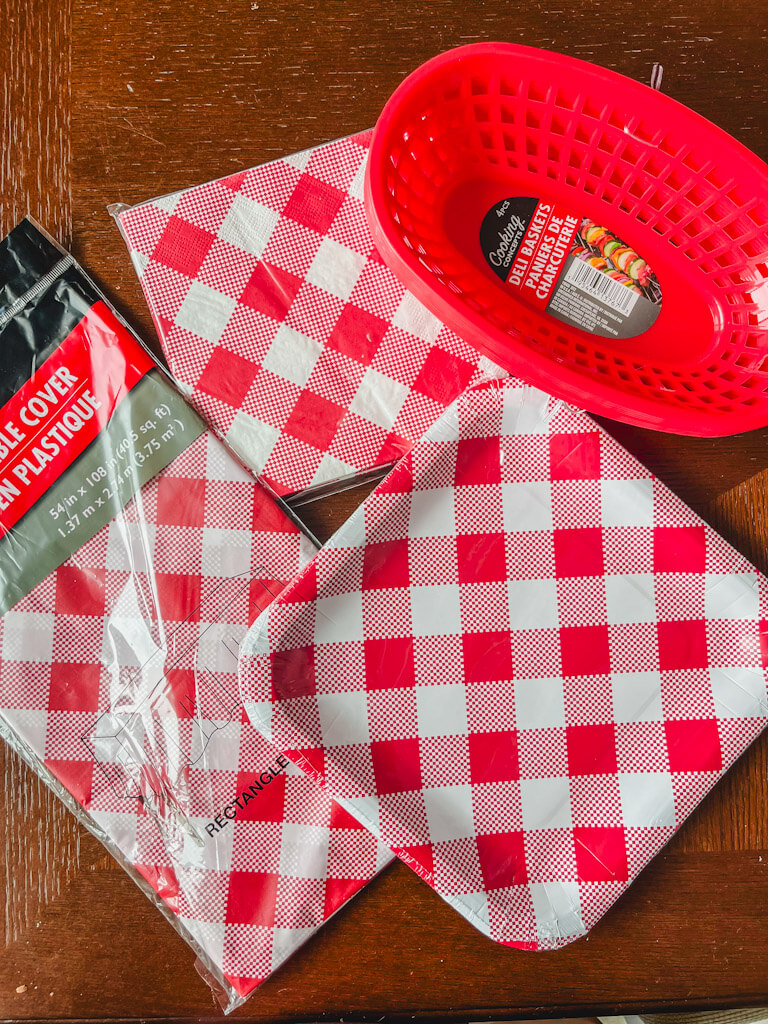 red and white gingham pattern napkins, plates, and tablecloth with red plastic food baskets next to them