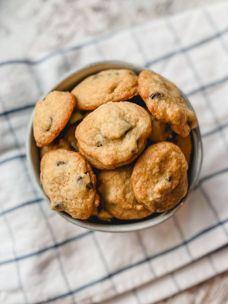 baked mini chocolate chip cookies in a small white bowl on top of a white tea towel.