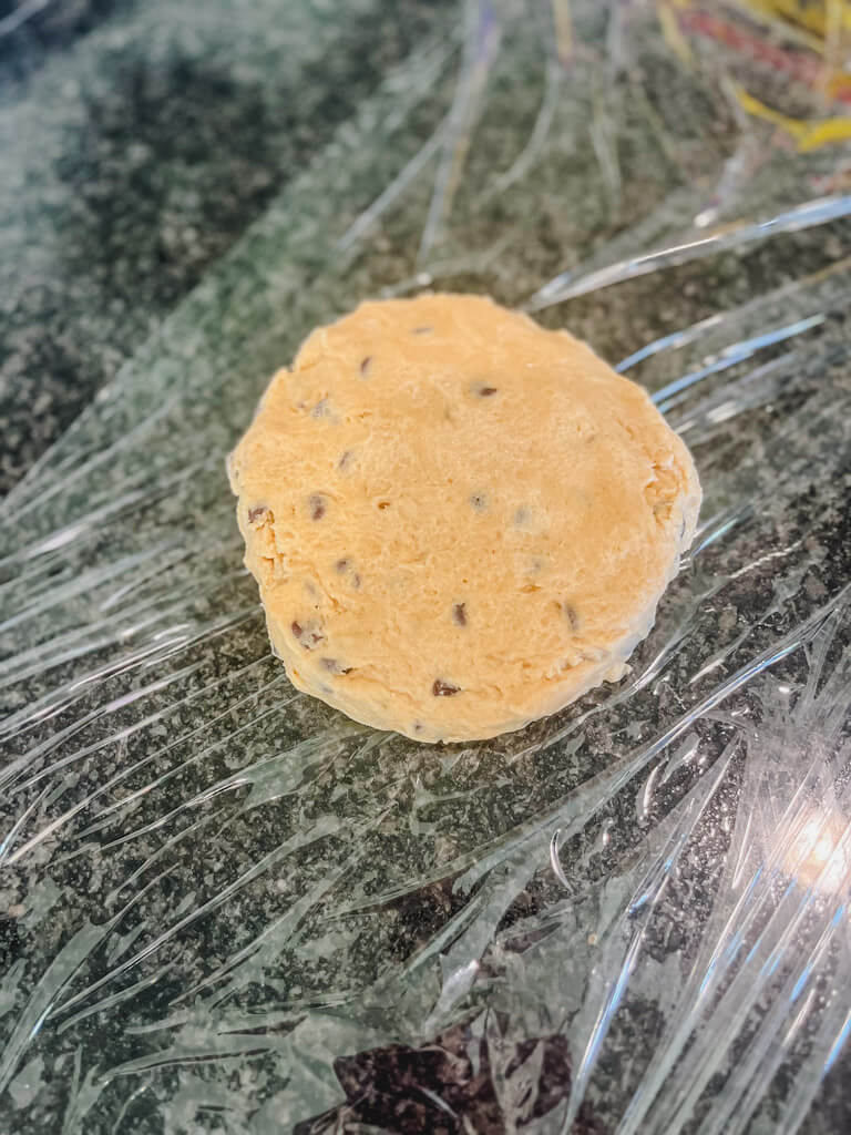 cookie dough that has been formed into a disc on top of plastic wrap ready to go into the freezer.