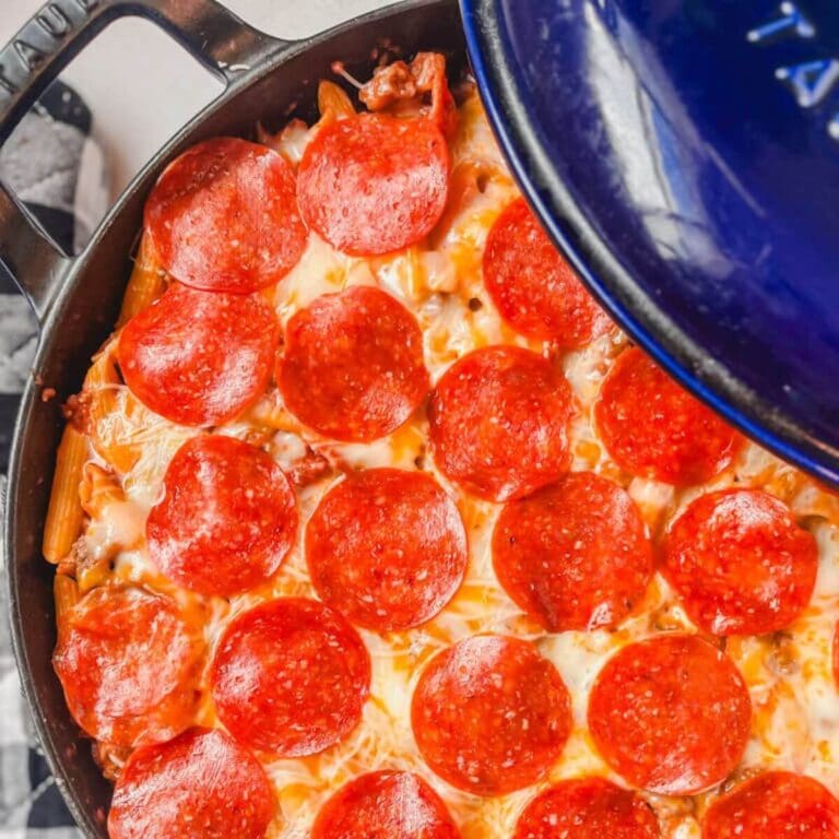 overhead picture of one pot pizza pasta in a blue cast iron skillet with a black and white oven mitt next to the pot.