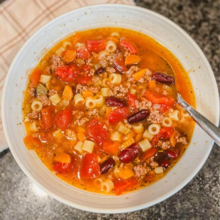 overhead image of instant pot pasta fagioli in a white bowl with a fabric napkin next to the bow.