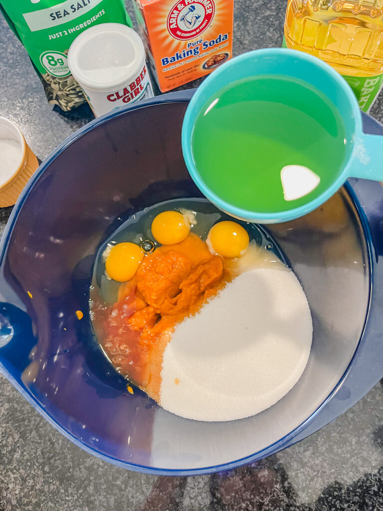 wet ingredients for pumpkin muffins being added to a blue mixing bowl.