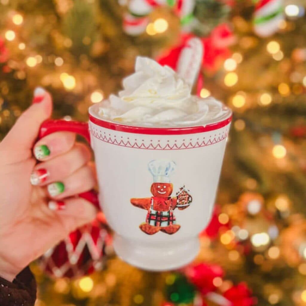 homemade stovetop hot chocolate in a Christmas mug being held in front of a Christmas tree.