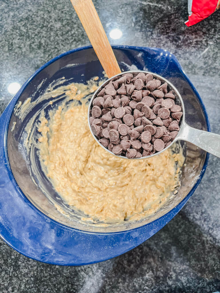 semi-sweet chocolate chips in a 1 cup measuring cup about to be added to the banana bread muffin top mixture.