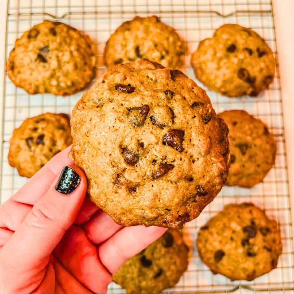 close up of a banana bread muffin top being held up over muffin tops resting on a wire rack.