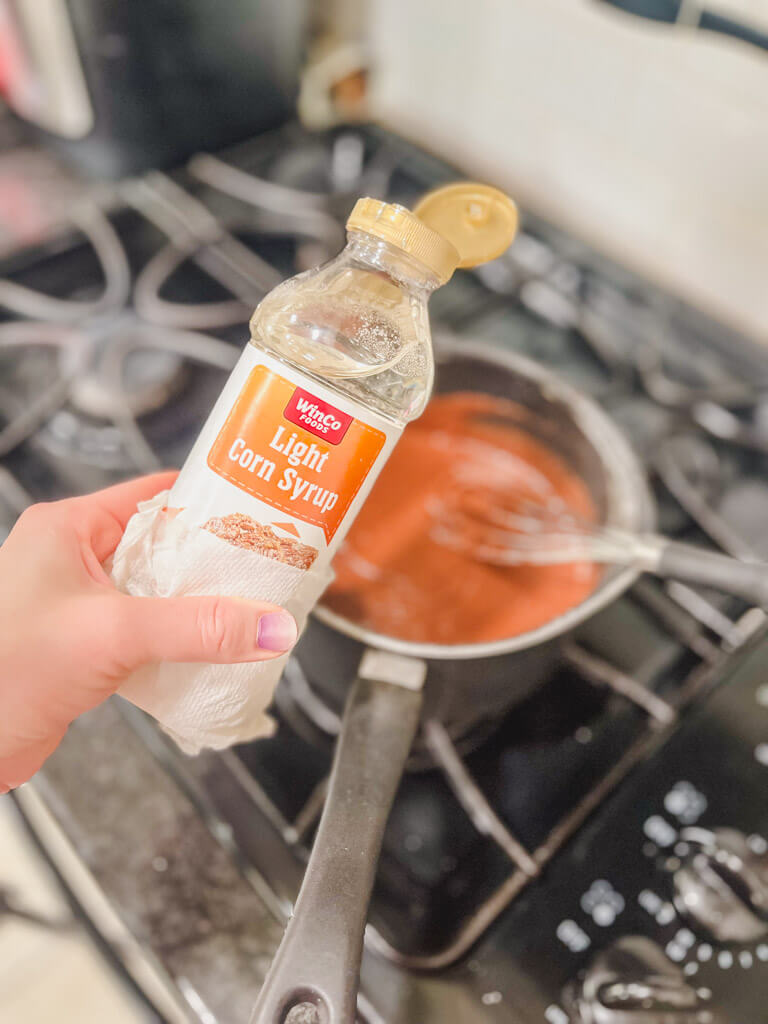 a bottle of corn syrup being held close to the saucepan to make our warm frosting.