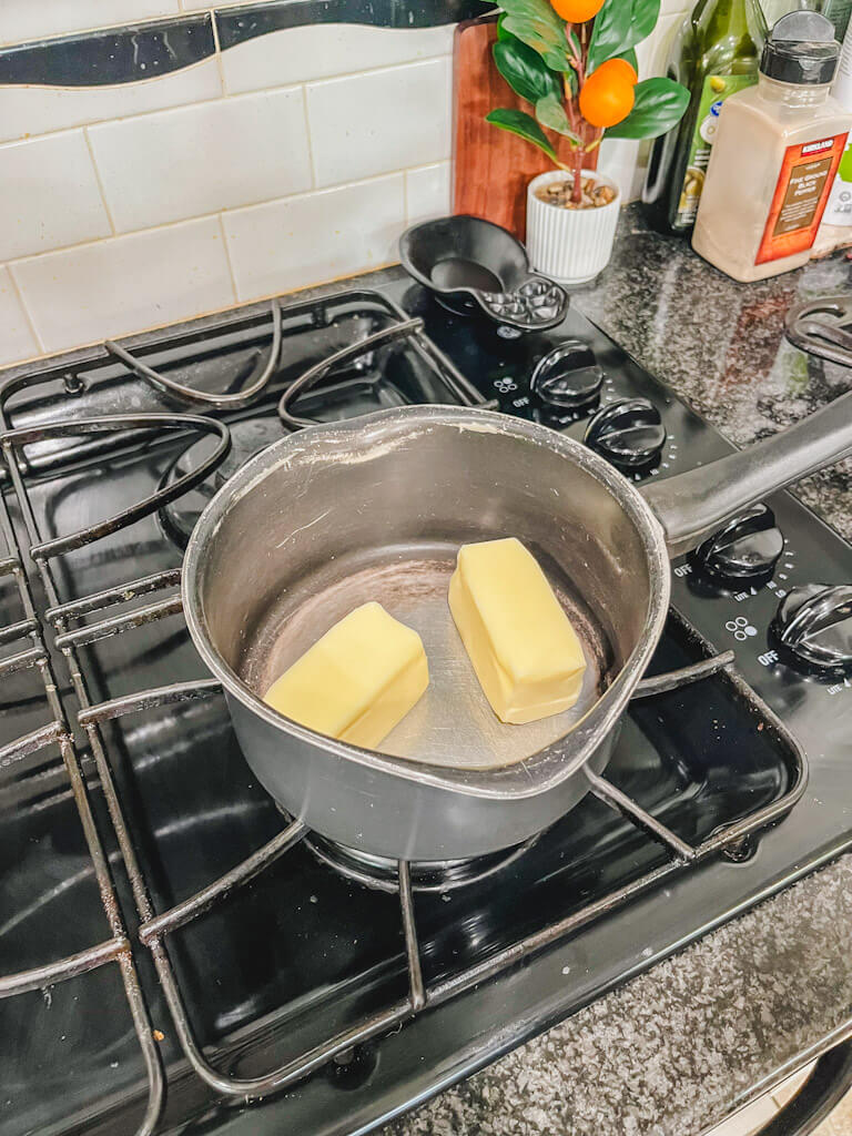 two sticks of butter melting in a saucepan on the stove top.