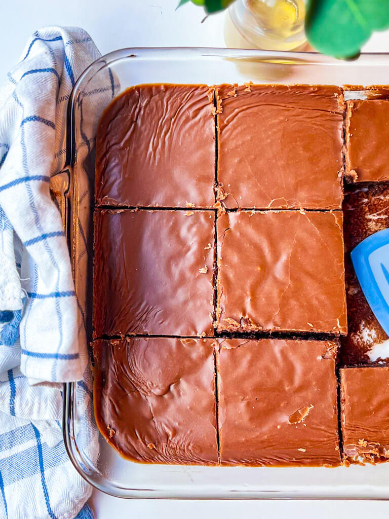 a baking dish with cut slices of buttermilk texas sheet cake next to a blue striped kitchen towel.