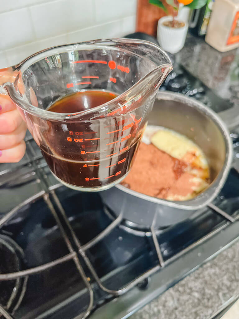 brewed coffee in a glass measuring cup about to be poured into the saucepan on the stove.