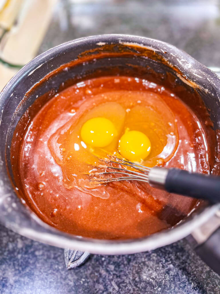 two eggs being added to the flour and cocoa mixture in the saucepan for our buttermilk texas sheet cake recipe.