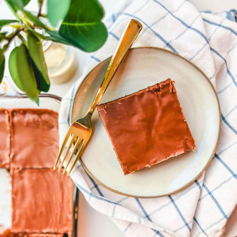 an overhead image of a slice of buttermilk texas sheet cake on a plate with a gold fork next to the cake.