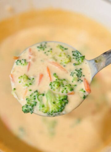 a close up of a ladle of Panera's copycat broccoli cheddar soup being held over a white pot of the soup.